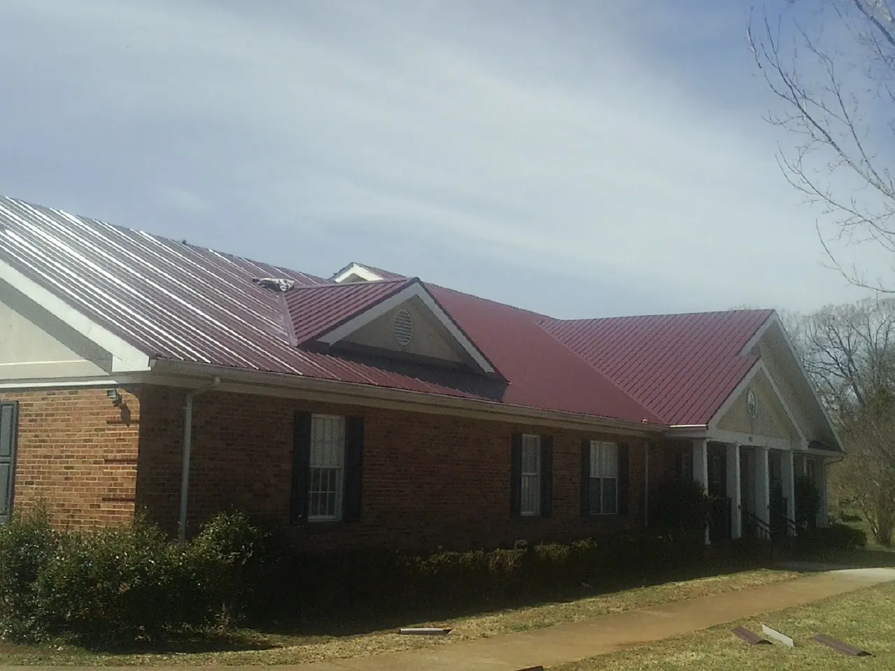 Red metal roof with gabled entries on a long brick building, from a Hail Damage Roof Repair job in Carthage