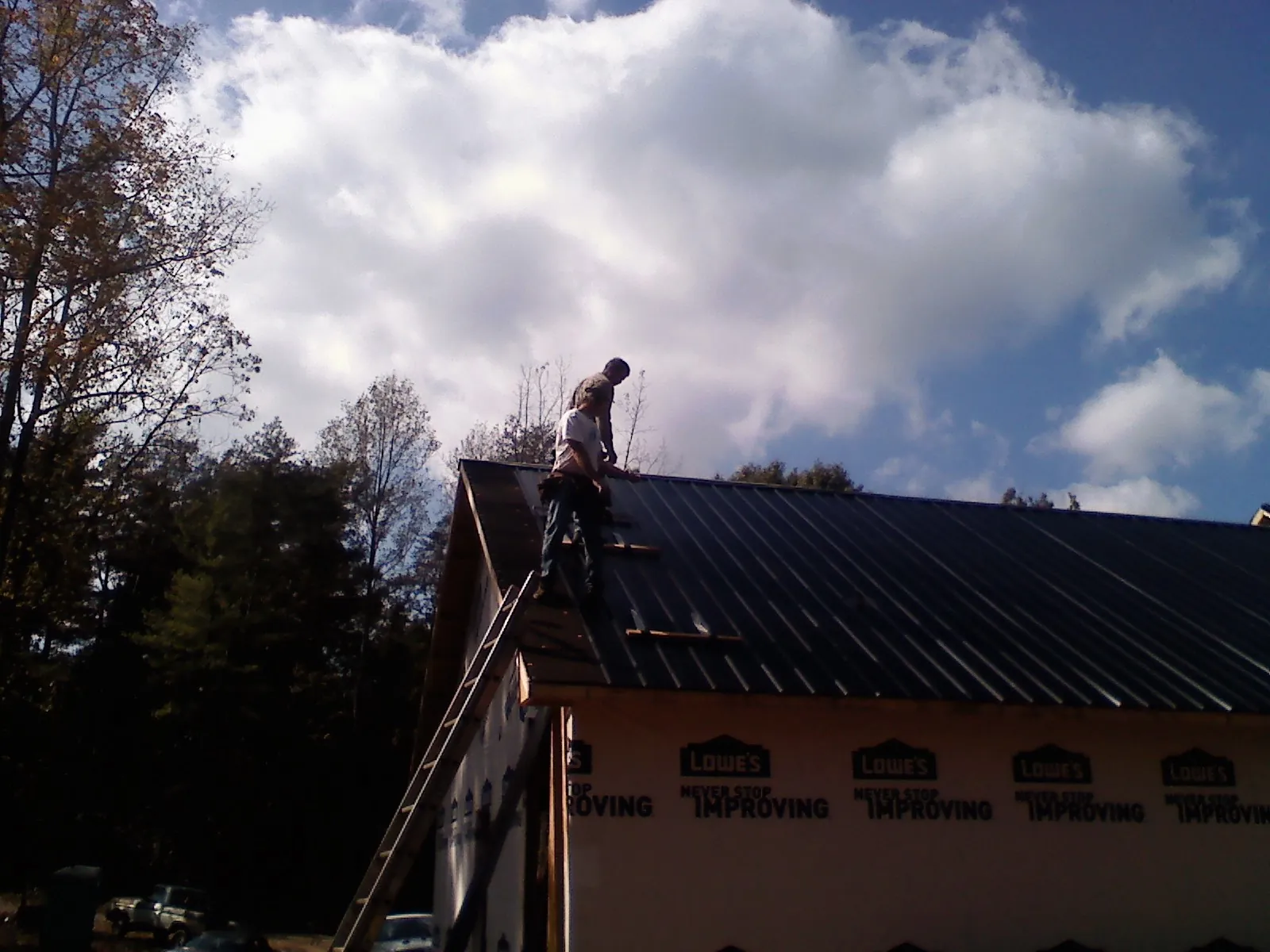 Roofer fastening dark metal panels high against a cloudy sky, from a Roof Inspection job in Carthage