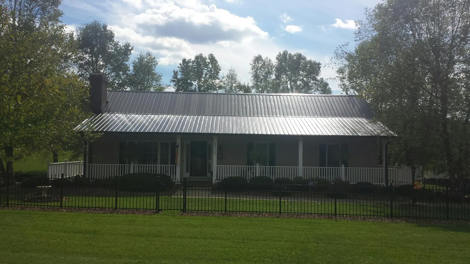 Gray metal roof on a brick ranch with a full width front porch — Gutter Guard Installation work by our crew in Carthage